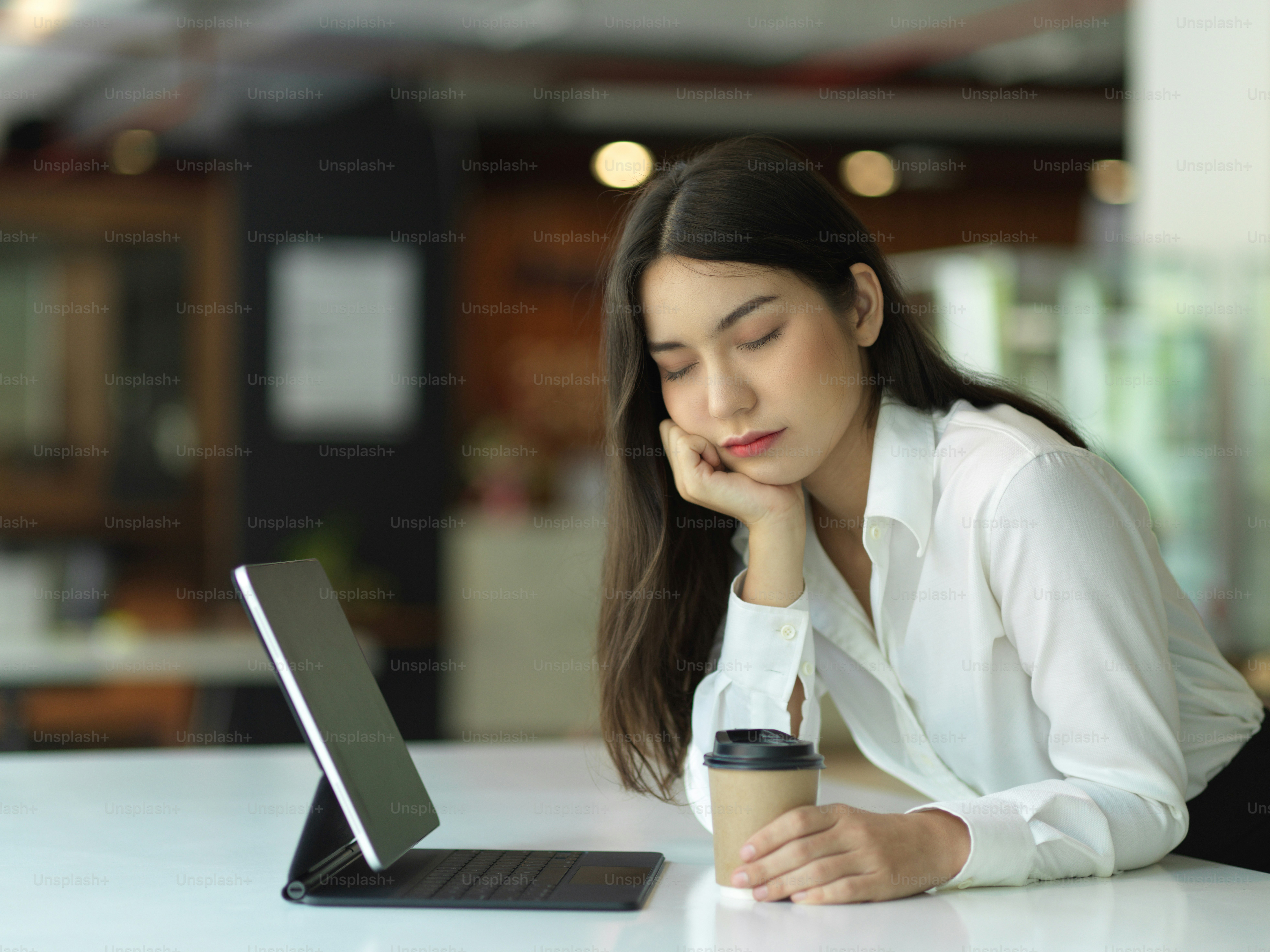 オフィスの机に座っている間、目を閉じた女性のオフィーワーカーの肖像画はリラックスしてコーヒーカップを持っていると感じています
