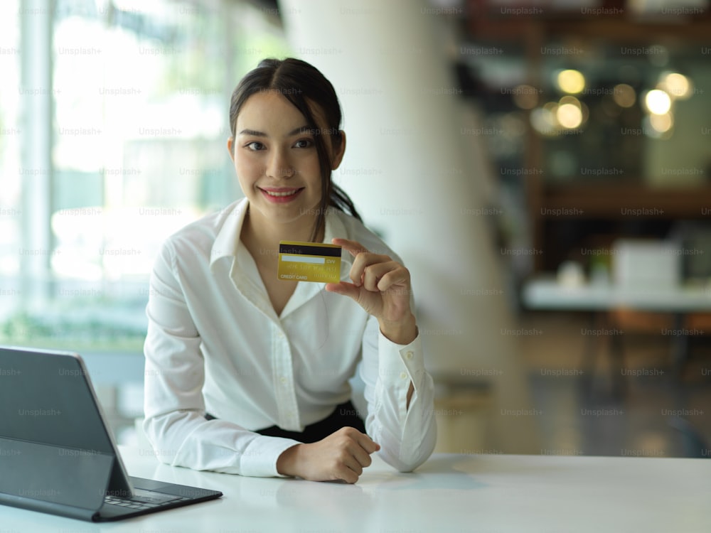Retrato de una mujer joven confiada que muestra la tarjeta de crédito y sonríe a la cámara, concepto de pago en línea