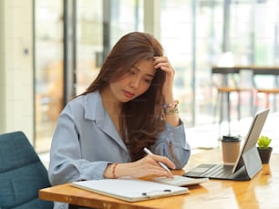 Porträt einer Geschäftsfrau, die sich bei der Arbeit mit Finanzpapieren und Taschenrechnern im Büroraum gestresst fühlt