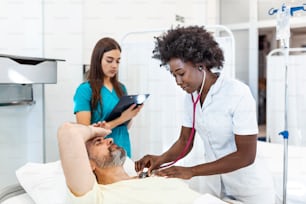 Hospitalized man lying in bed while doctor checking his pulse. Doctor and nurse examining senior male patient in hospital room.