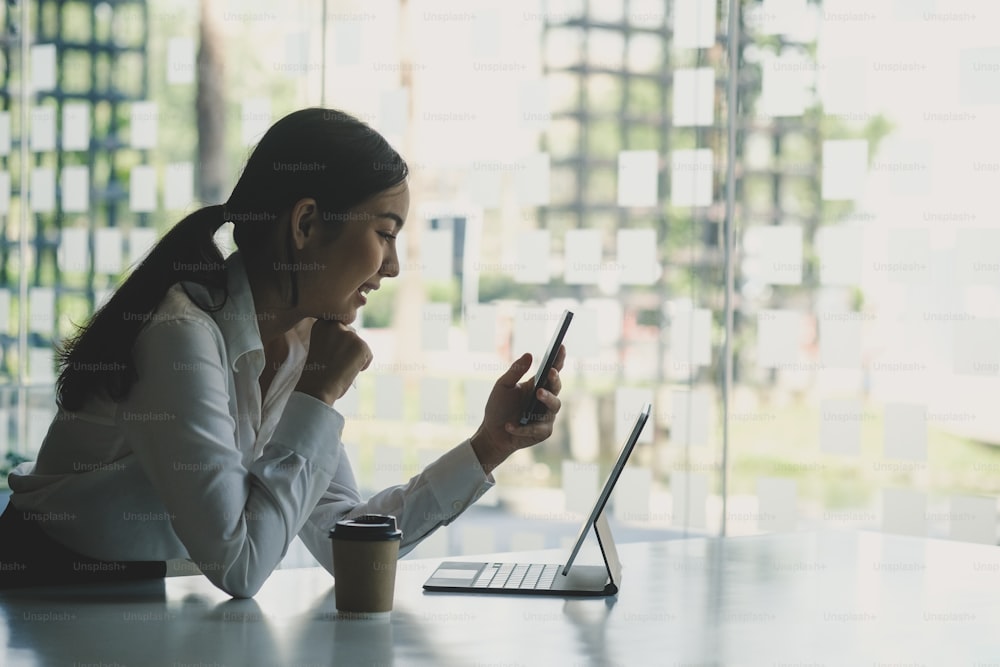 Side view of young woman office worker taking a break at office and using mobile phone.