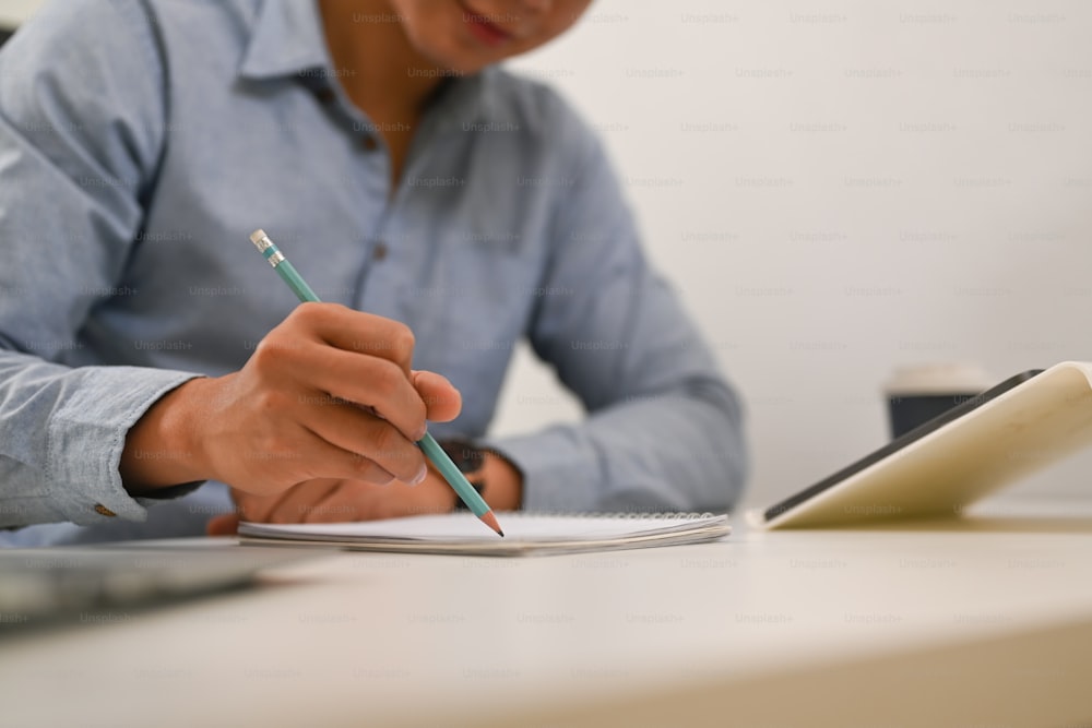 Foto cortada de empresário segurando lápis escrevendo no caderno de anotações na mesa do escritório.