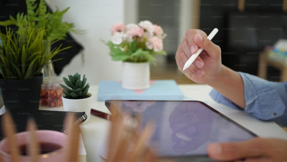 Vista de perto do homem segurando caneta stylus e tablet digital com tela em branco no local de trabalho confortável.