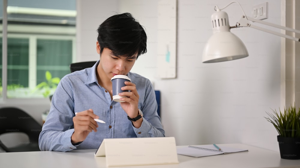 Empresário atraente bebendo bebida quente e trabalhando com tablet digital.