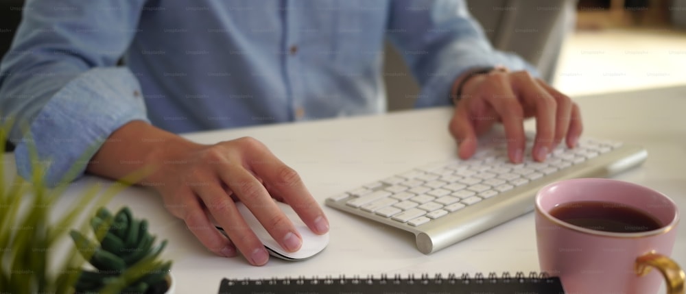 Imagem horizontal do homem designer gráfico mão digitando no teclado sem fio no local de trabalho moderno.