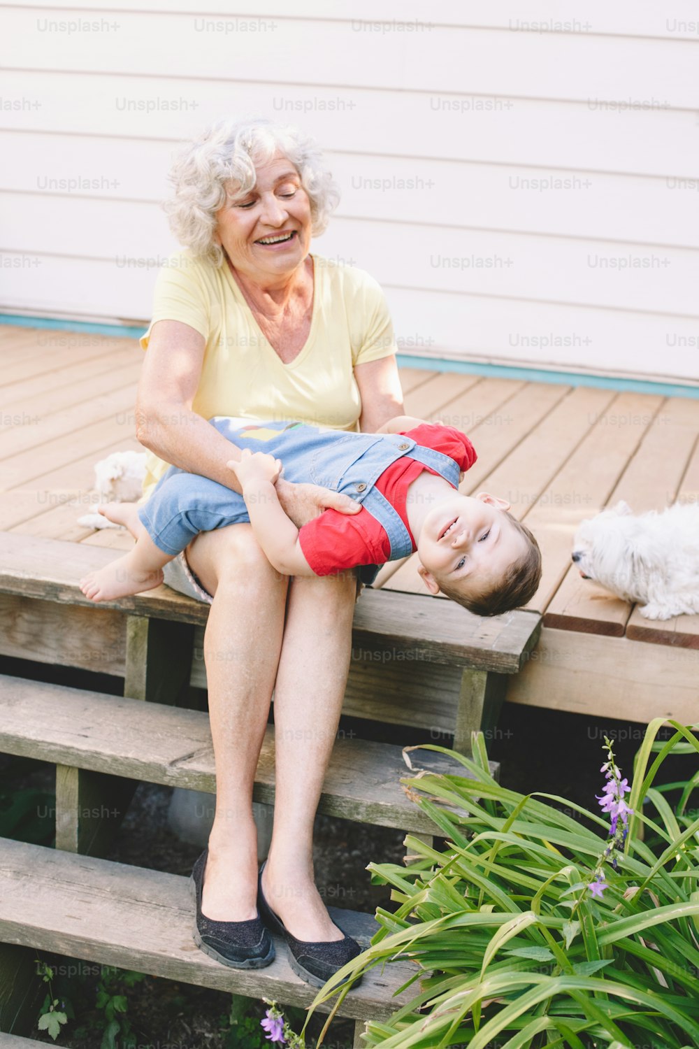 Grandmother playing with grandson boy on porch at home backyard. Bonding of relatives and generation communication. Old woman with baby having fun spending time together outdoor.