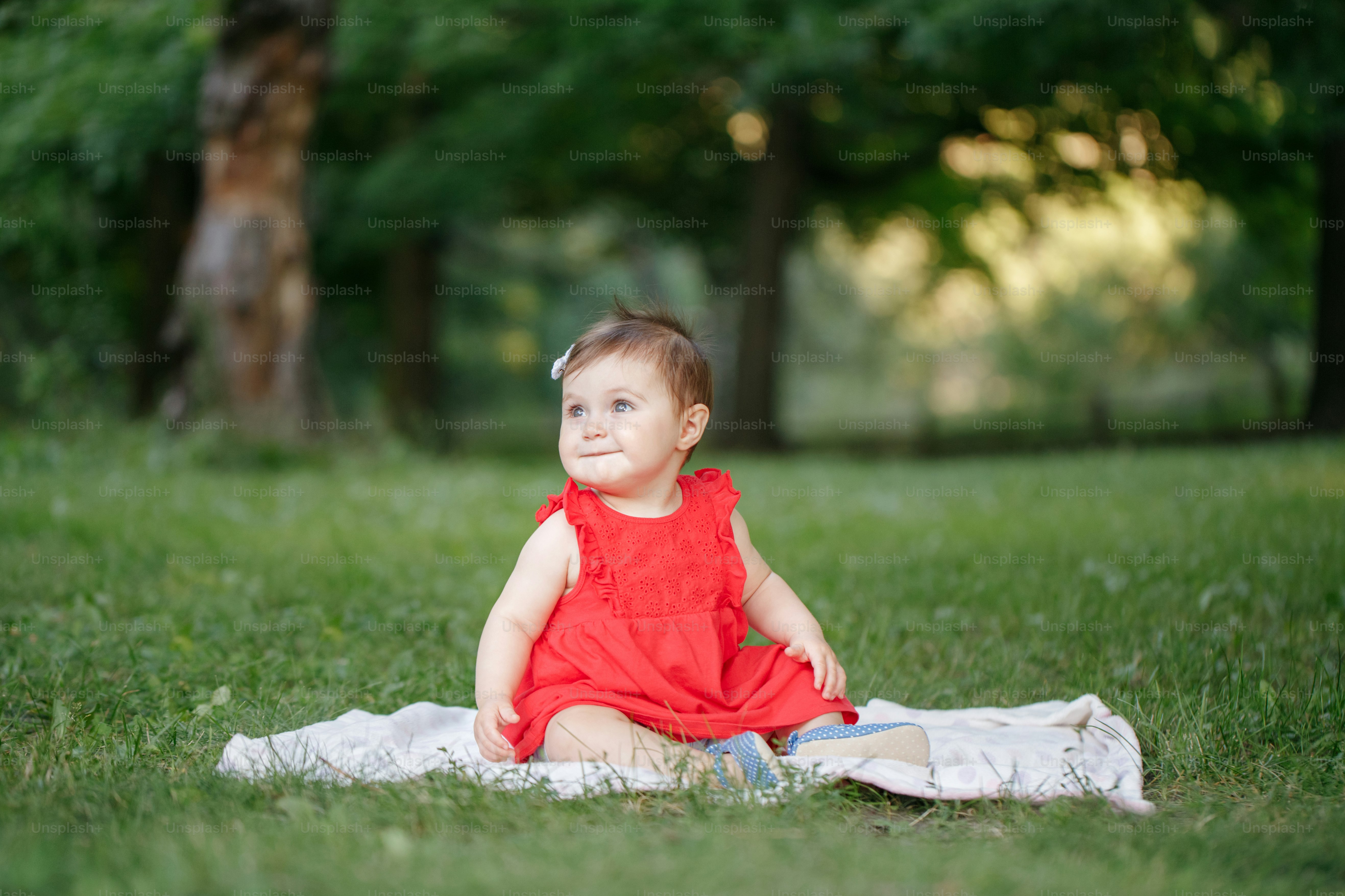 Bambina adorabile carina in vestito rosso seduta su coperta bianca nel parco all'aperto. Bambino divertente che gioca e si diverte in una giornata estiva all'aperto. Ragazzo divertente. Stile di vita autentico, infanzia felice.