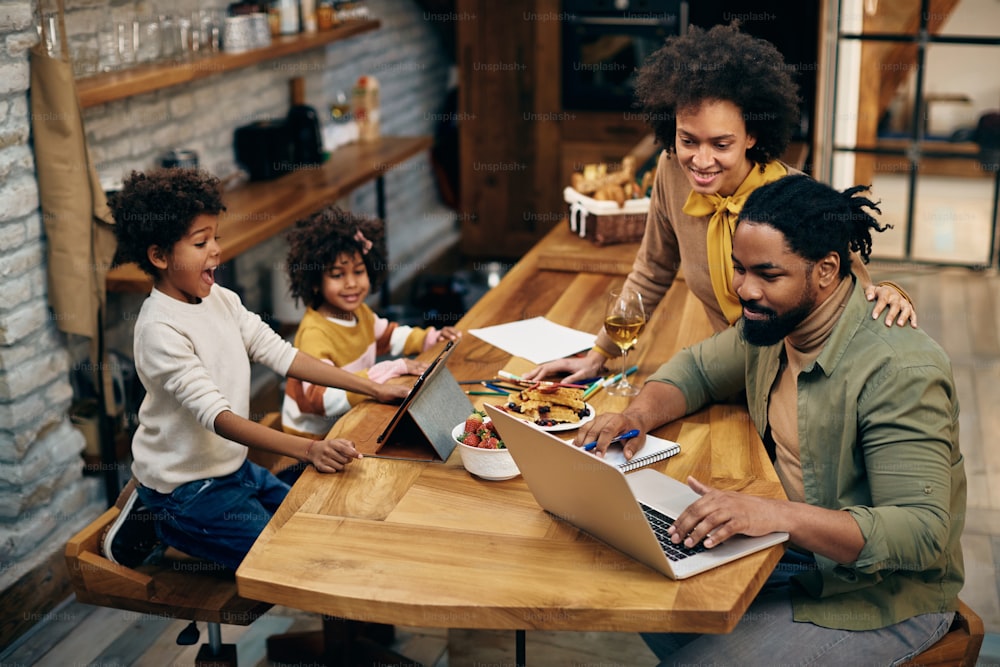 African American parents working on laptop while their children are using digital tablet at home.