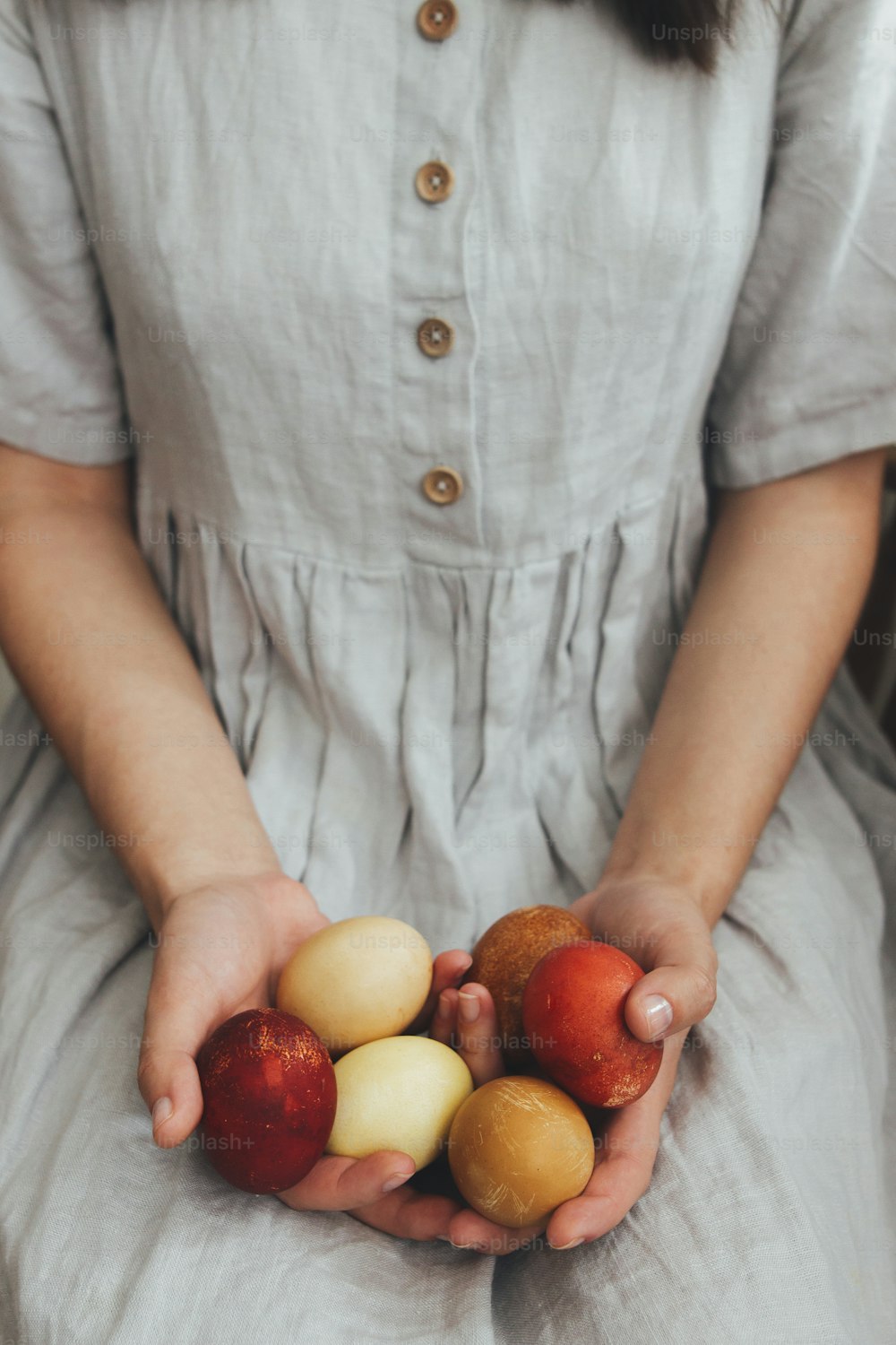 Happy Easter! Woman in rustic linen dress holding natural dyed easter eggs in hands. Natural painted eco red and brown eggs. Aesthetic holiday, stylish image