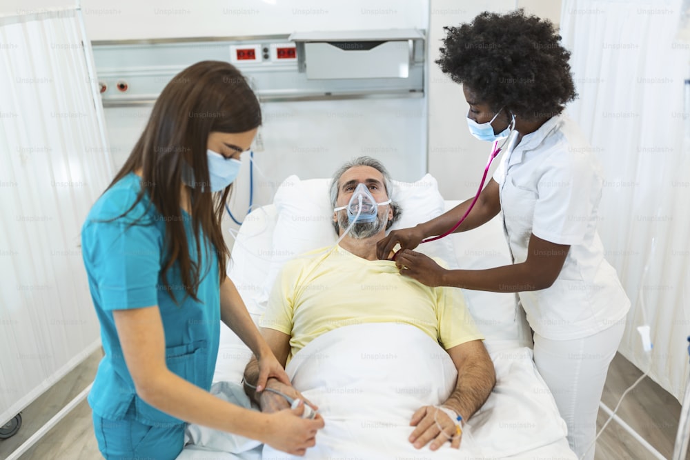 防護マスクを着用した医師が、感染した高齢の患者を病院で診察しています。病院では、高齢の患者が酸素マスクを着けてベッドに横たわって休んでいます。
