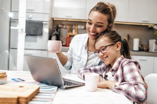 Madre feliz con su hija pequeña disfrutando de las compras en línea o trabajando desde casa. Negocios a distancia y comunicación virtual con familiares y amigos.