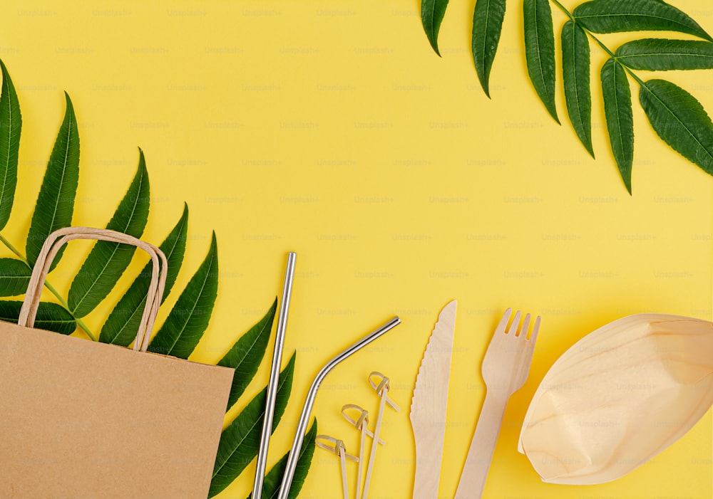 Eco friendly set with bamboo, paper disposable tableware and metal straws on yellow background. Copy space, flat lay