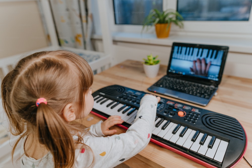 Little girl watching online lesson tutorial how to learn a synthesizer indoor.
