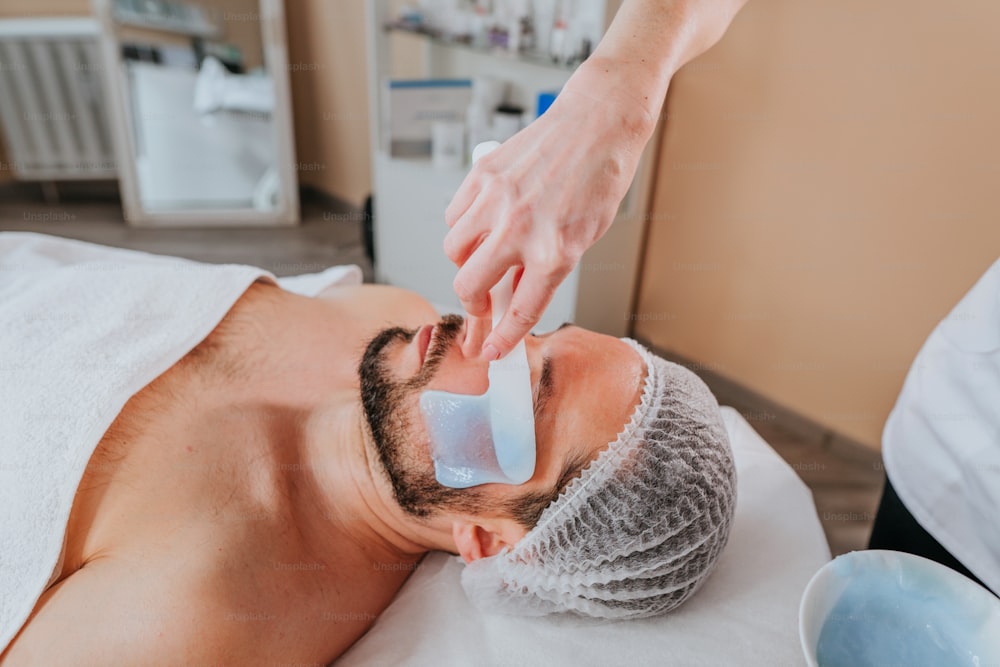 Esthetician making facial cleansing procedure using algae mask for a man in the beauty salon