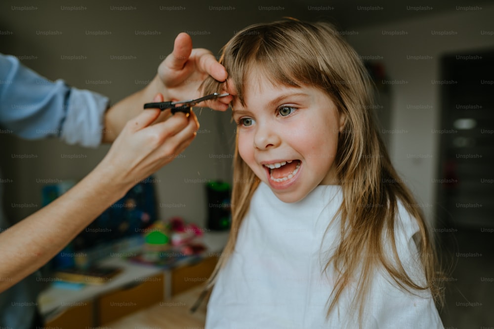 Primer plano de las manos de una madre femenina cortando el cabello de su hija de cuatro años en casa en la habitación de los niños. Rutina diaria en casa.