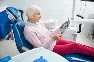 歯科用椅子で待っている間、歯のX線写真を保持してチェックする年金生活の女性