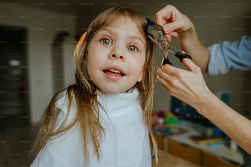 Close-up das mãos da mãe cortando o cabelo de sua filha de quatro anos em casa no quarto das crianças. Rotina diária em casa.