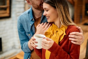 Mujer sonriente disfrutando en una taza de café mientras su novio le muestra afecto.