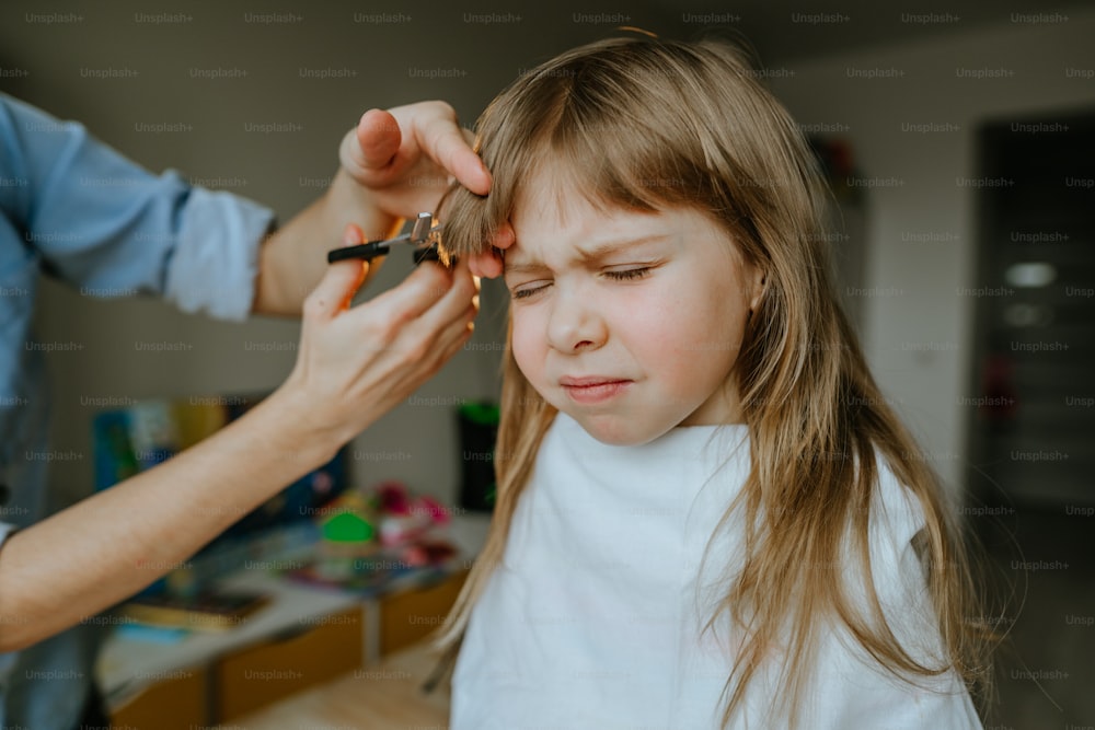 Primer plano de las manos de una madre femenina cortando el cabello de su hija de cuatro años en casa en la habitación de los niños. Rutina diaria en casa.