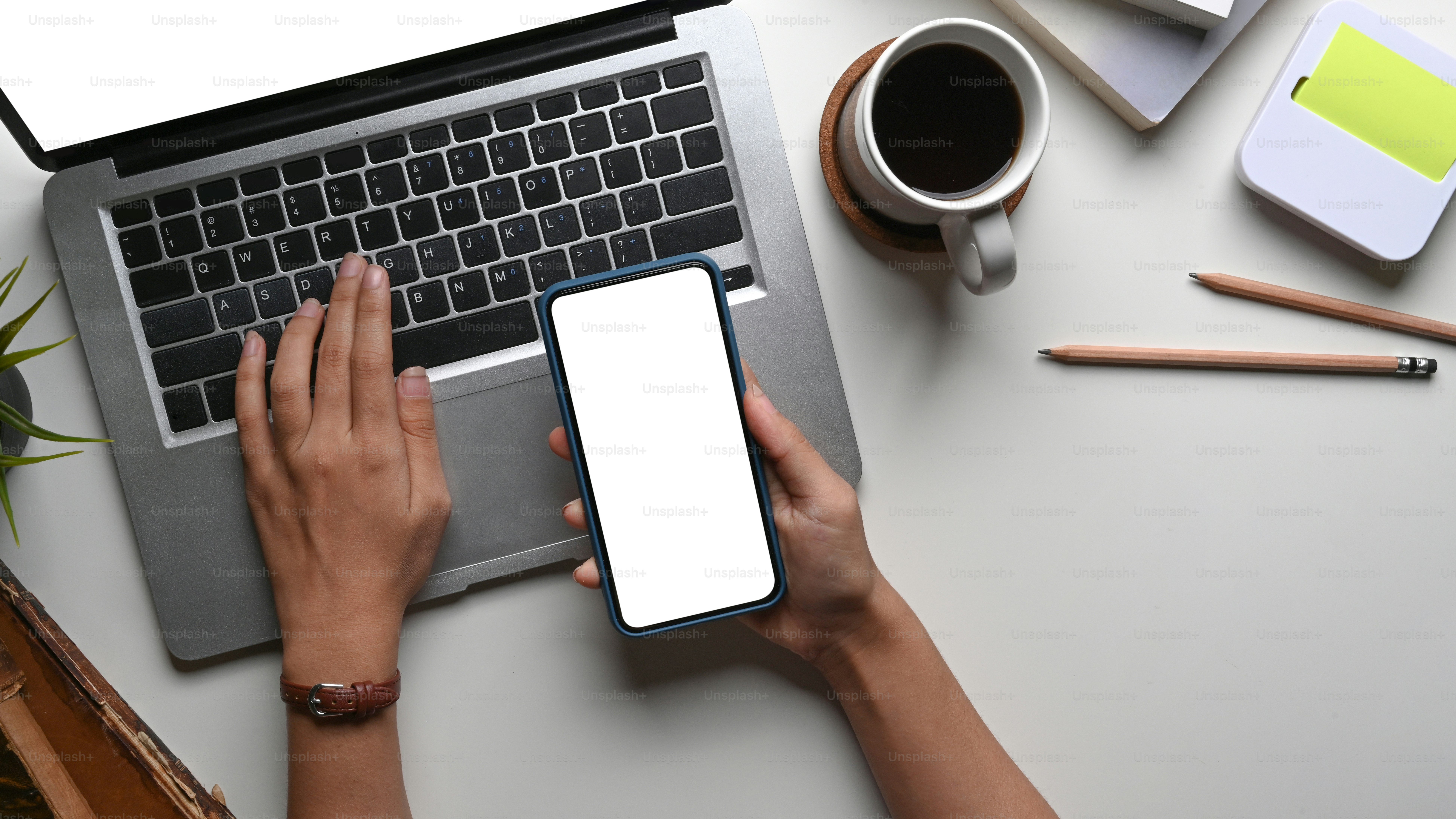 Overhead view of woman holding smart phone and working on laptop computer at office desk.