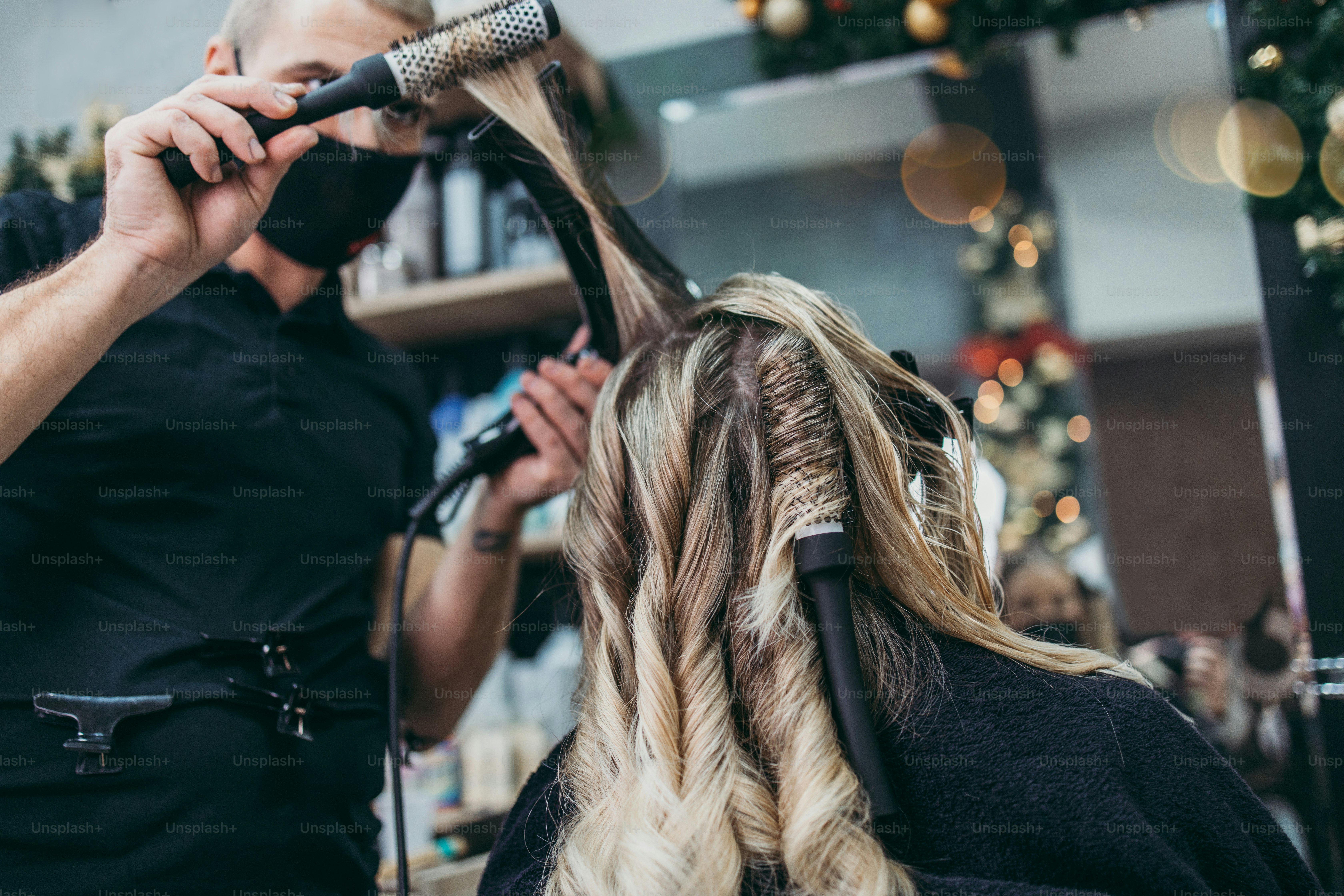 Un parrucchiere che usa una spazzola rotonda per acconciare i capelli biondi di un cliente in un salone