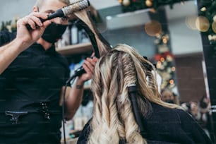 Beautiful hairstyle of woman after dyeing hair and making highlights in hair salon. She is wearing protective face mask as protection against virus pandemic.