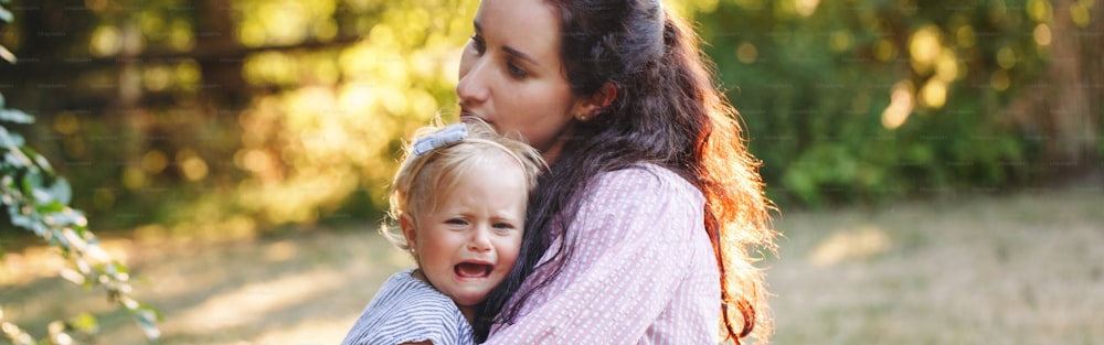 Mother hugging pacifying sad upset crying toddler girl. Family young mom and crying baby in park outdoor. Bonding relationship of mom and child baby. Family together protection. Web banner header.