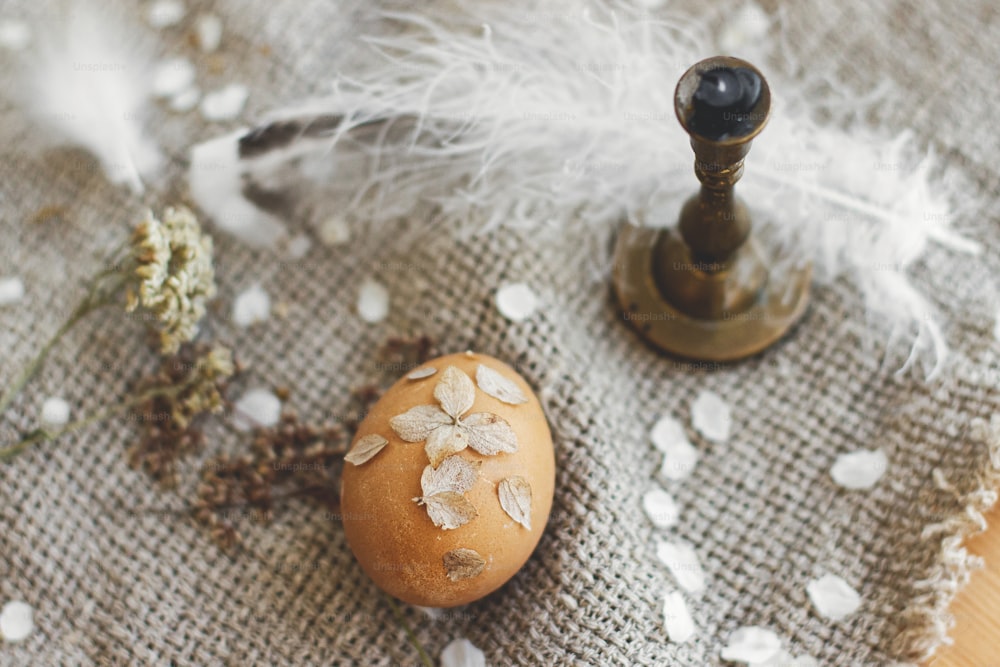 Uovo di Pasqua decorato con petali di fiori secchi su sfondo di tovagliolo di lino rustico, candela e piuma. Arredamento creativo naturale ed ecologico di uova di Pasqua. Buona Pasqua