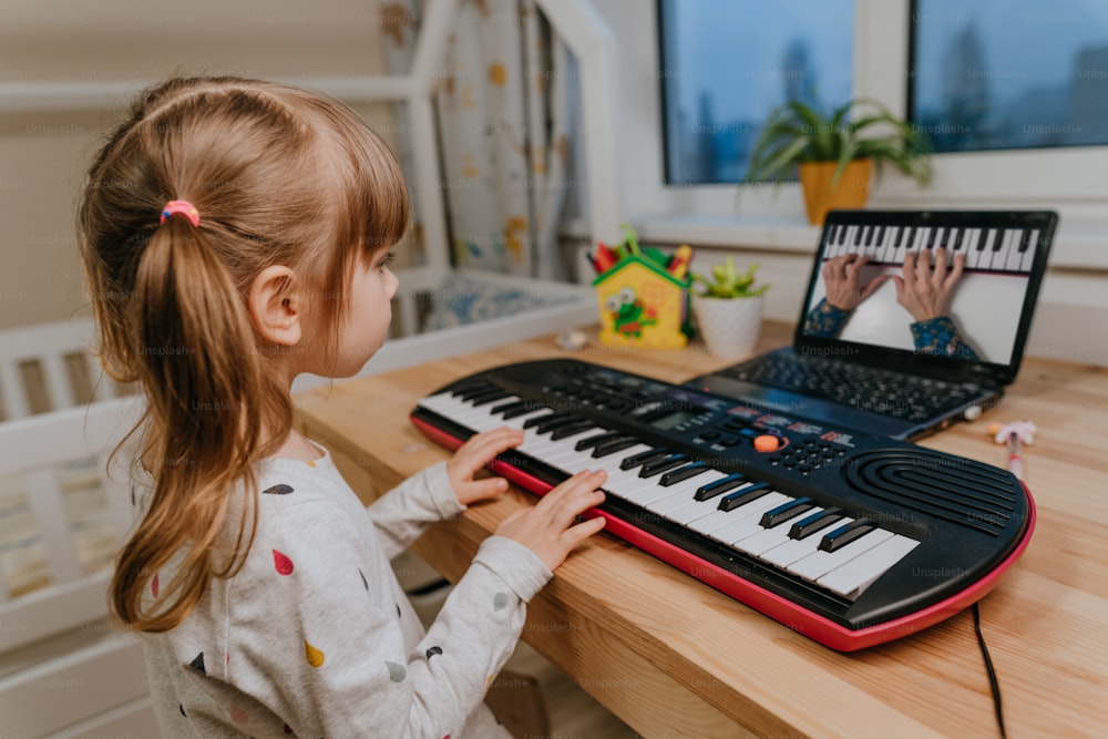 Little girl watching online lesson tutorial how to learn a synthesizer indoor.