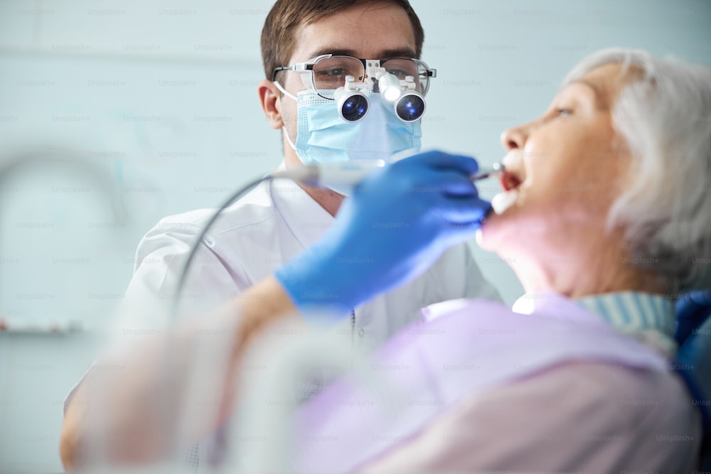 Zahnarzt kümmert sich um die Mundhöhle älterer Bürger mit einem Stahlbohrer am Handstück, das an den Zähnen arbeitet
