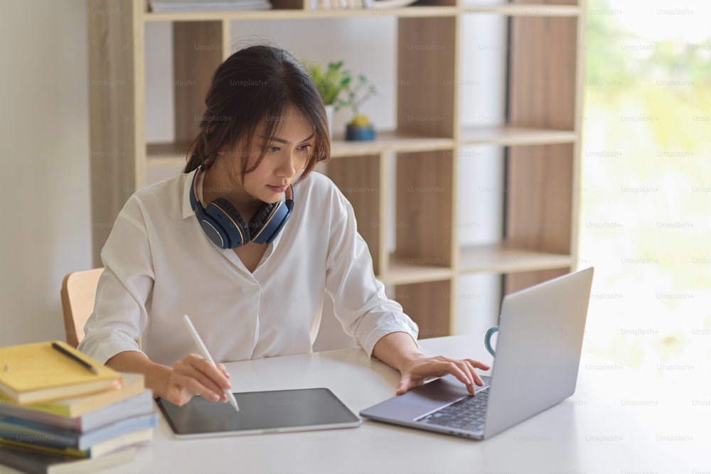 Portrait d’une travailleuse active travaillant avec une tablette numérique et un ordinateur portable dans un bureau à domicile