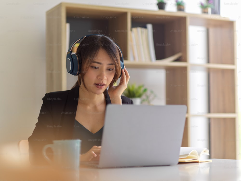 Retrato da empresária que trabalha em casa, usando fone de ouvido e laptop na sala do escritório em casa