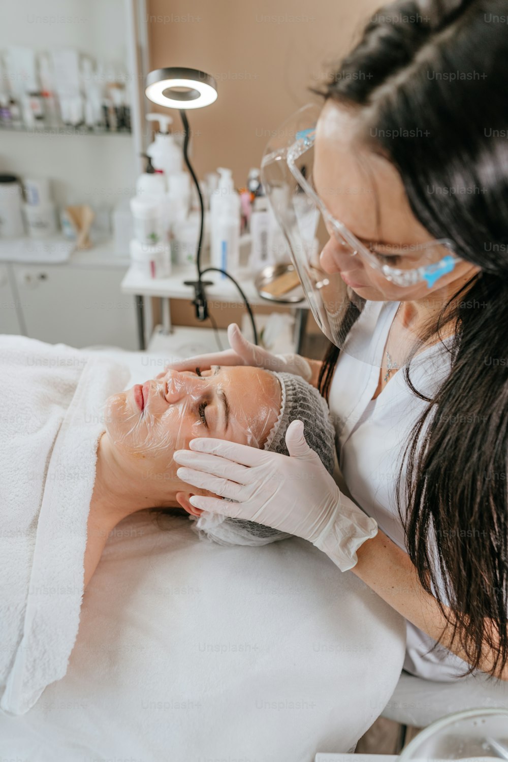 Esthetician or facialist making facial cleansing procedure to a woman in a beauty salon
