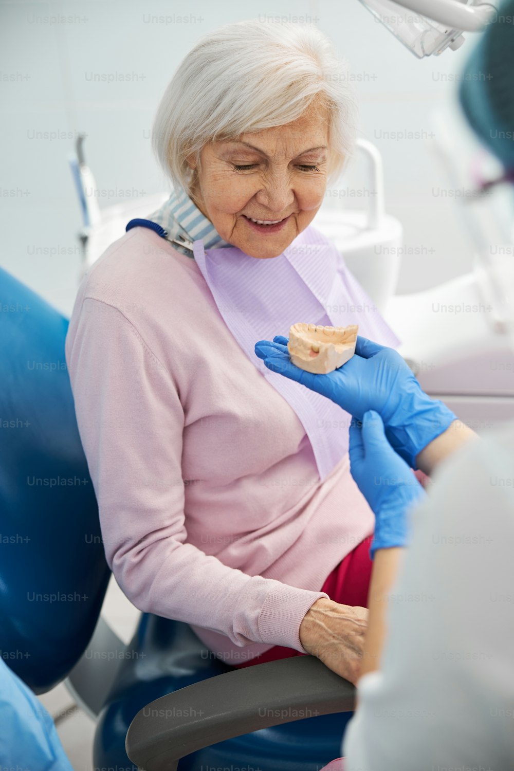 Mandíbula inferior moldeada en una mano en el guante del dentista frente a una anciana