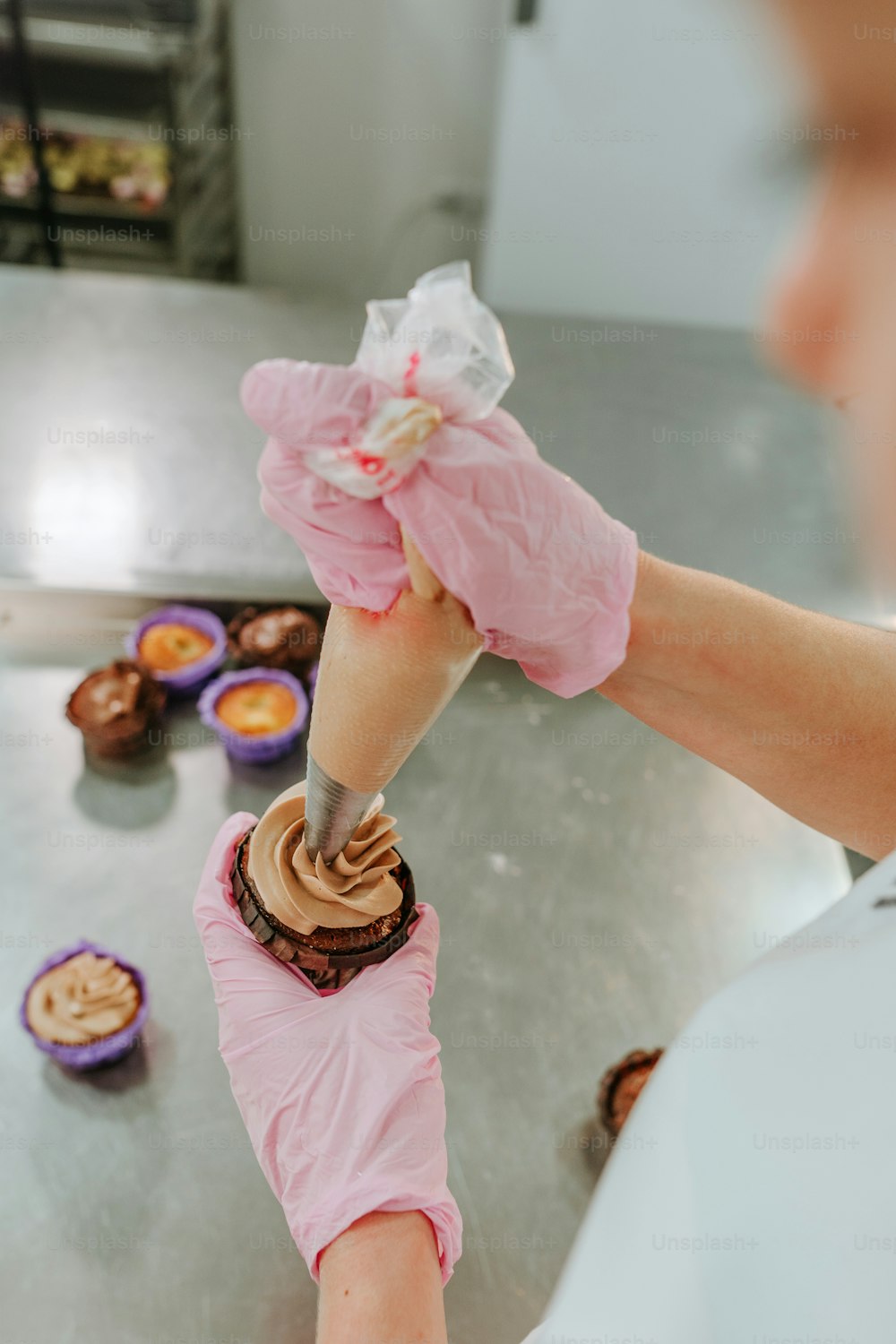 製菓スタジオでクリーム入りのペストリーバッグを使用してカップケーキを作るピンクの手袋をはめた女性菓子の接写