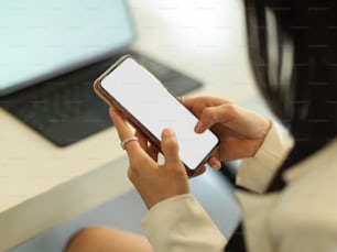 Cropped shot of businesswoman hands texting on mock up smartphone while sitting at workplace, clipping path