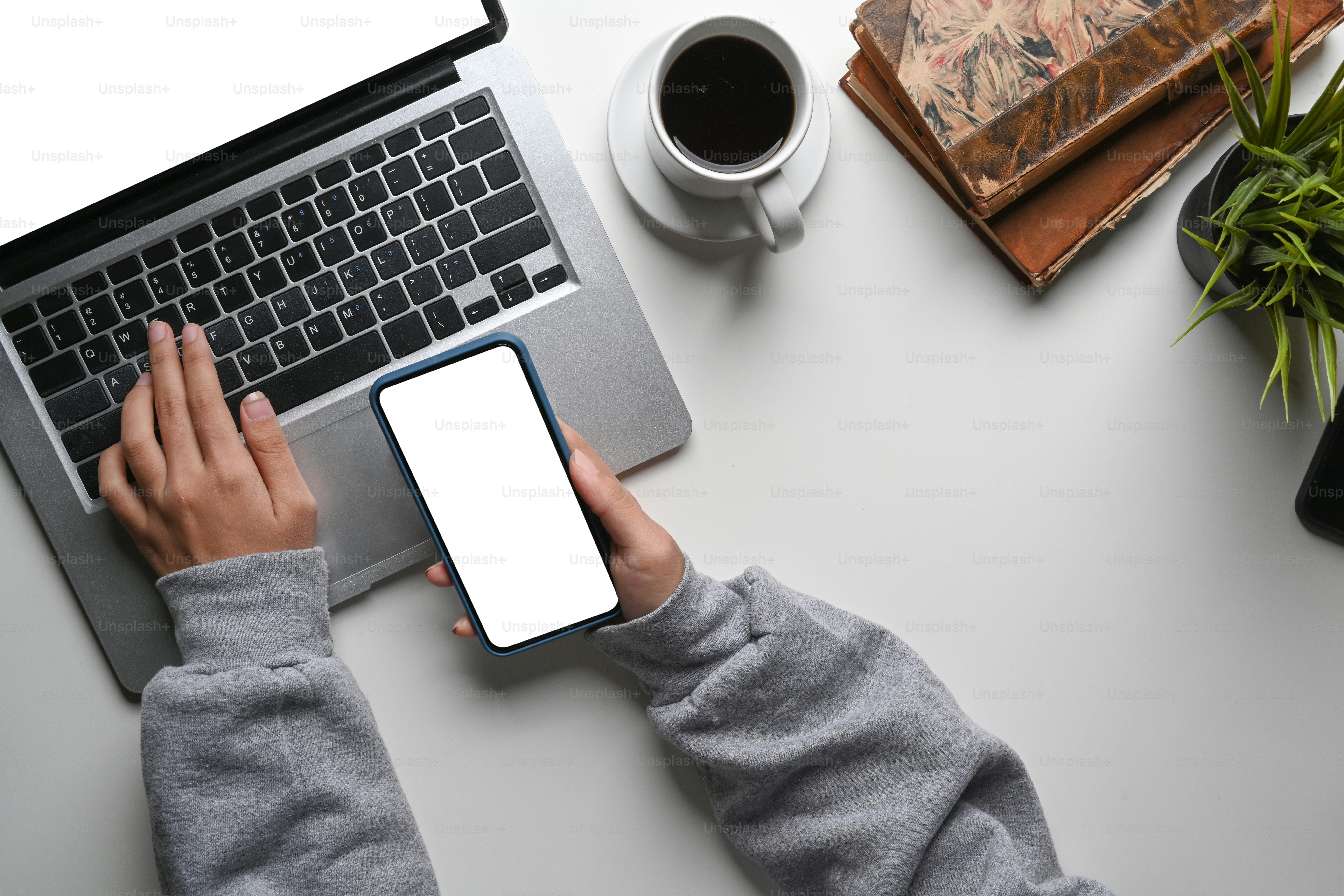 Above view of young woman holing mobile phone and working with laptop computer on white office desk.