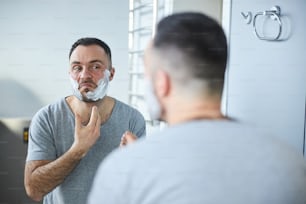 Handsome gentleman looking in the mirror and preparing skin for shaving