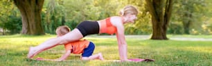 Family summer outdoor sport activity. Caucasian mother with child toddler boy doing workout yoga in park. Woman doing physical exercises together with kid son. Banner header for website.