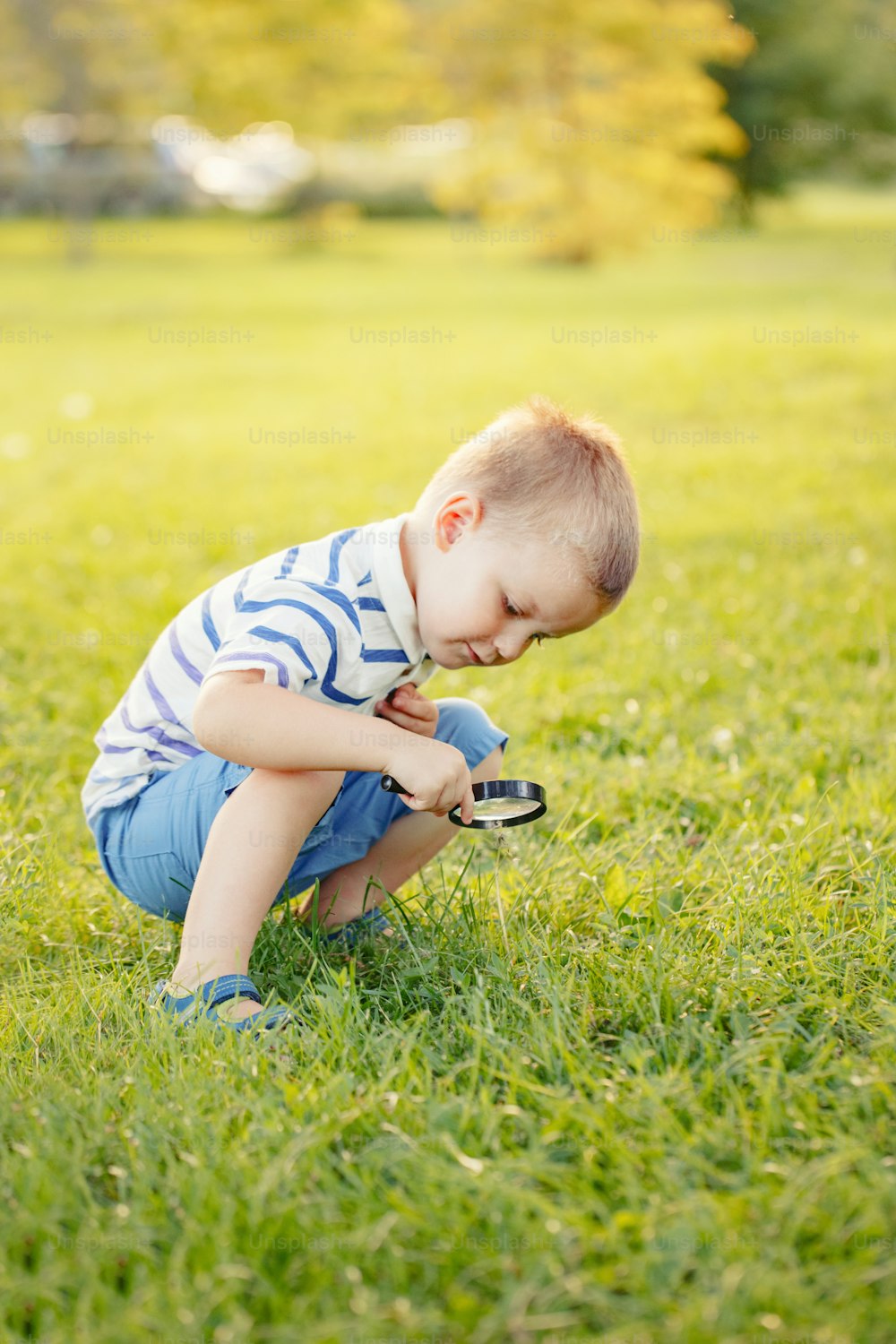 Bonito adorável menino caucasiano criança olhando para plantas grama flor no parque através de lupa. Garoto com lupa estudando aprendendo a natureza lá fora. Conceito de educação em ciências naturais infantis.