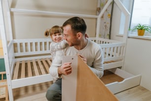 Little 4-years girl helps her father assemble or fixing the drawer of bed in the kids bedroom.