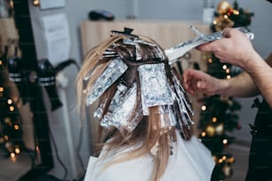 El peluquero tiñe el cabello femenino, haciendo reflejos para su cliente con una lámina. Llevan mascarilla protectora como protección contra la pandemia del virus.