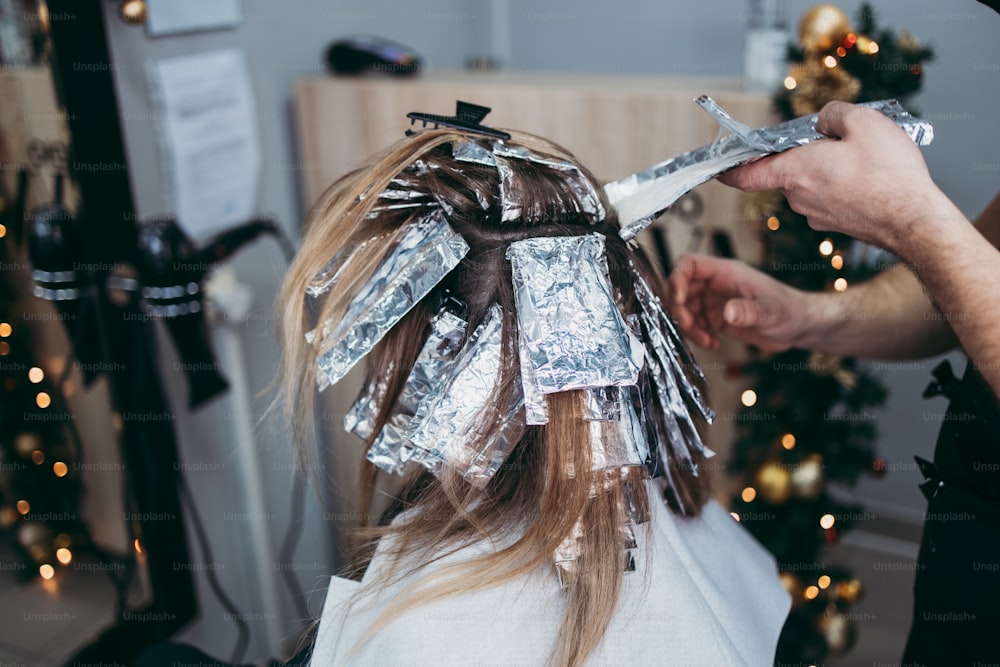 Hairdresser is dyeing female hair, making hair highlights to his client with a foil. They are wearing protective face mask as protection against virus pandemic.