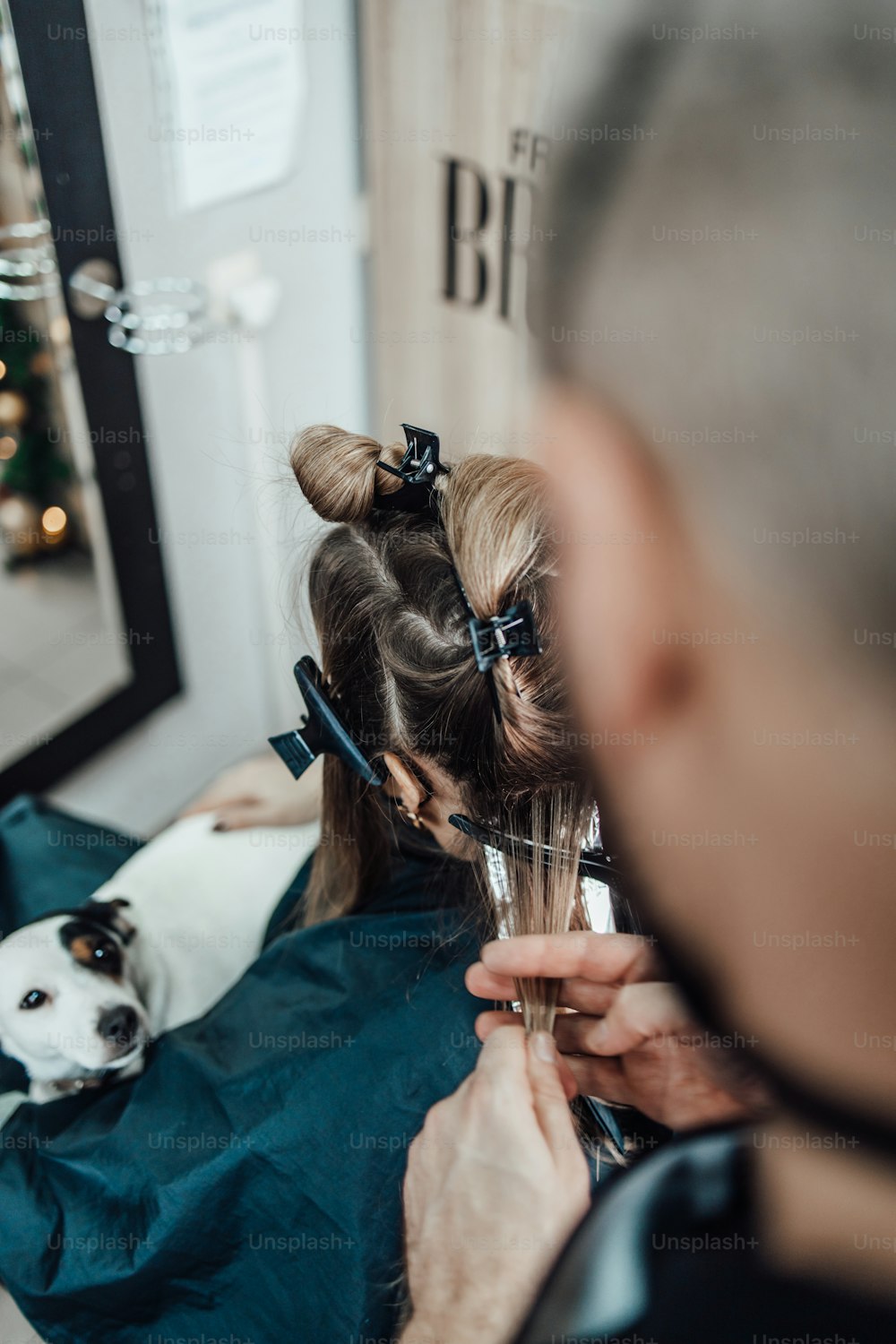 Hairdresser is dyeing female hair, making hair highlights to his client with a foil. They are wearing protective face mask as protection against virus pandemic.