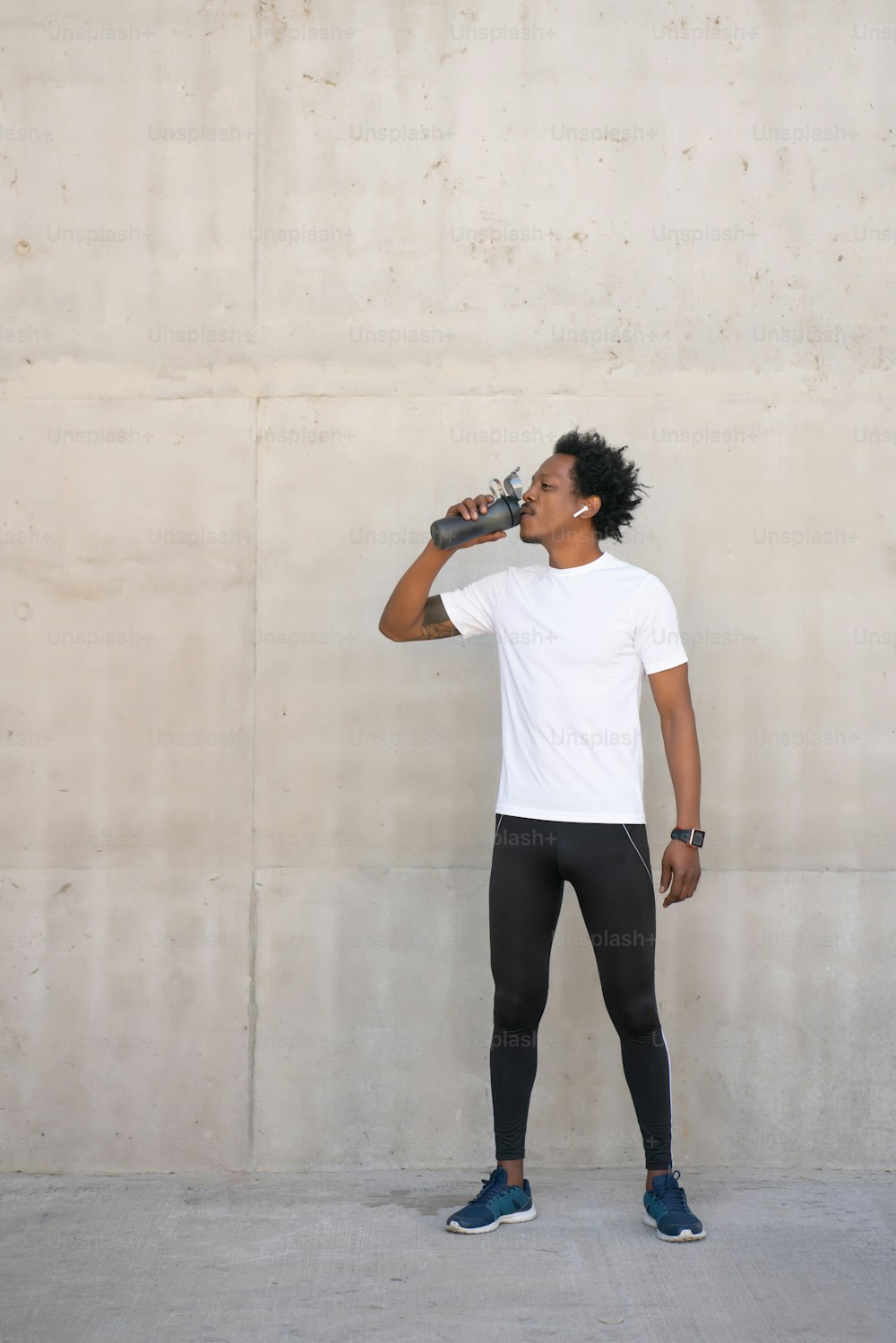 Uomo atletico afro che beve acqua e si rilassa dopo l'allenamento all'aperto. Concetto di sport e stile di vita sano.