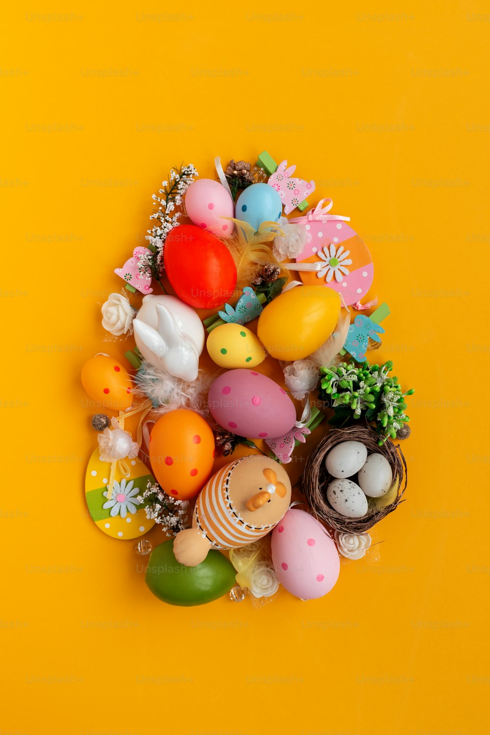 Easter egg shape made of colorful spring flowers and eggs on yellow background.  Easter celebration concept. Top view. Flat lay