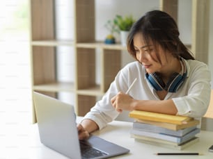 Portrait of female university student online studying with laptop and books in living room at home
