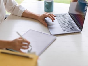 Side view of a woman working with laptop and digital tablet on white table in home office