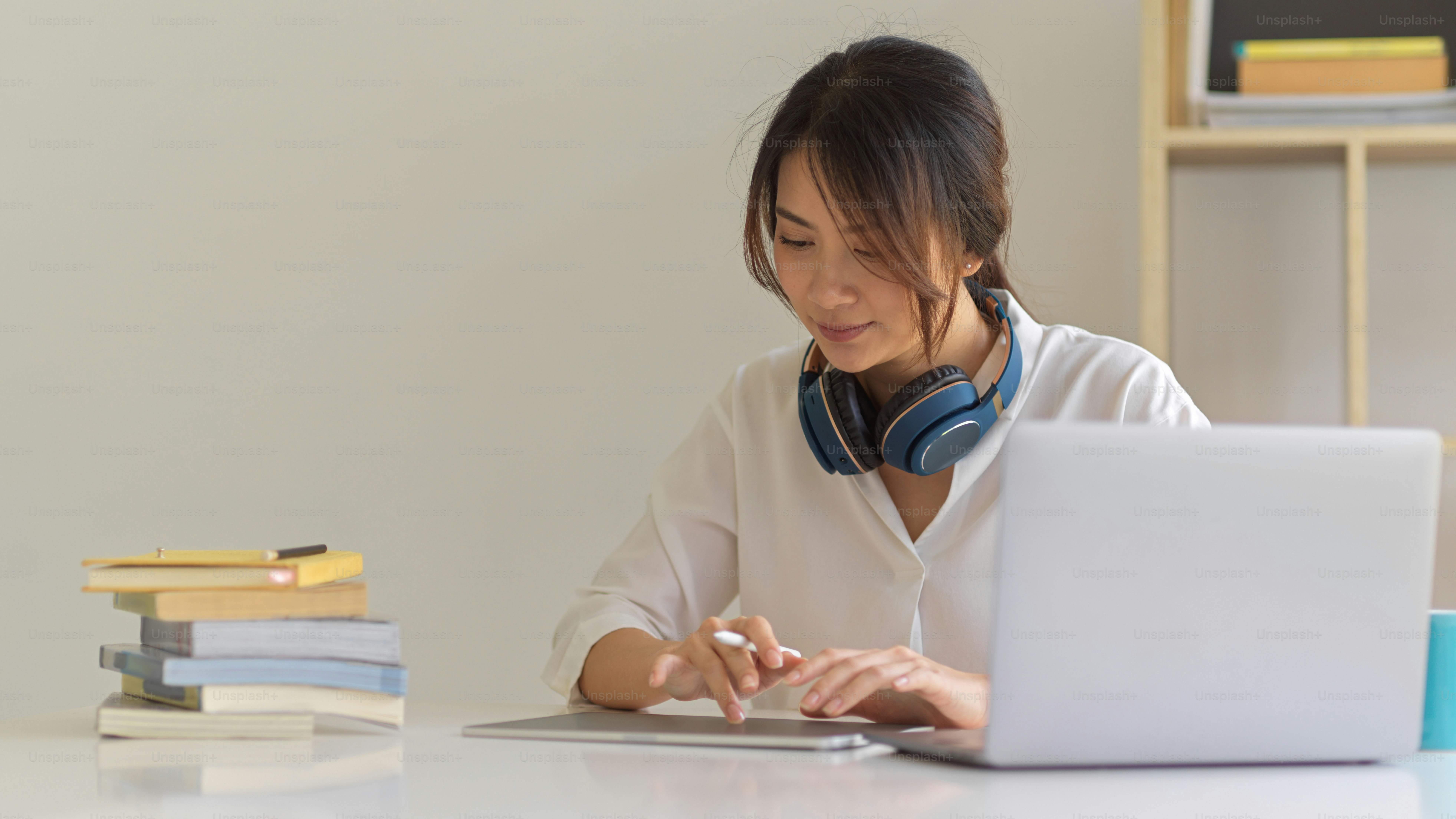 Potret mahasiswi yang berkonsentrasi pada tugasnya dengan tablet digital, laptop, dan buku
