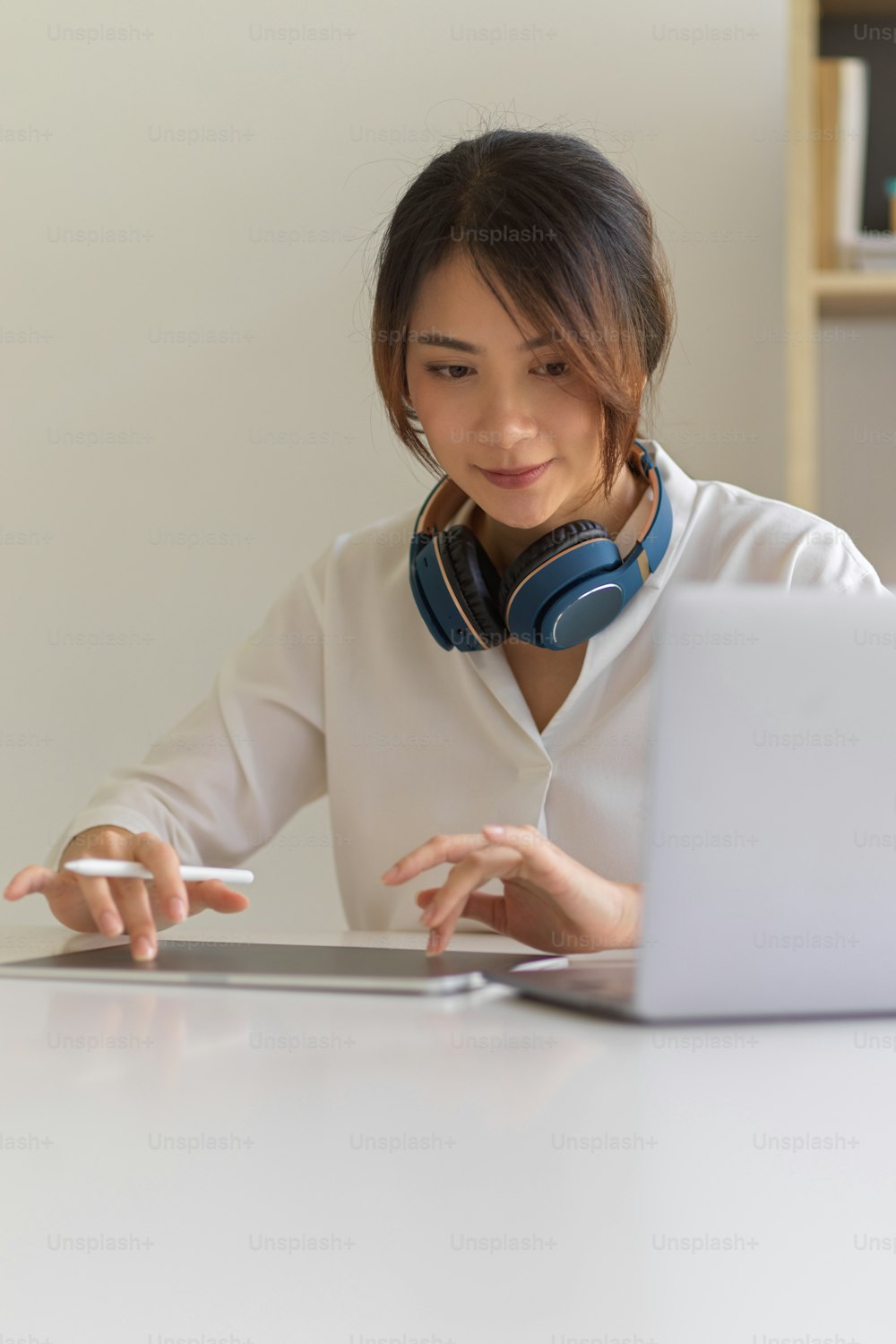Ritratto di una donna con la cuffia che lavora con il computer portatile e il tavolo digitale sulla scrivania bianca